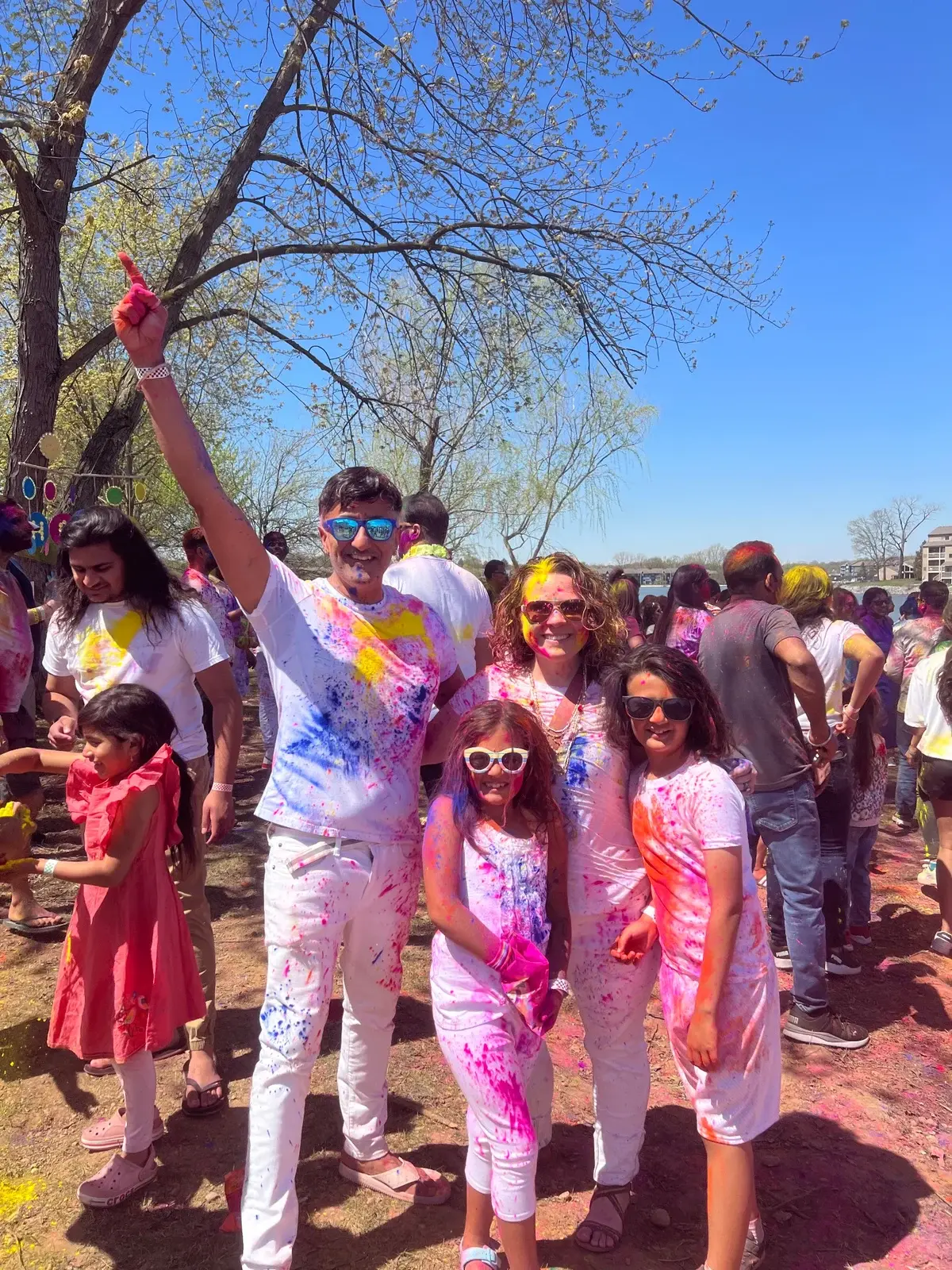 Neo celebrating Holi outdoors with adults and children covered in colorful powder
