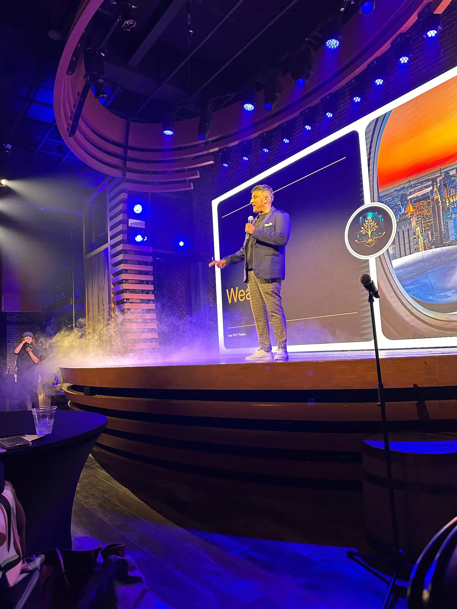 Neo speaking on a stage lit in blue and violet